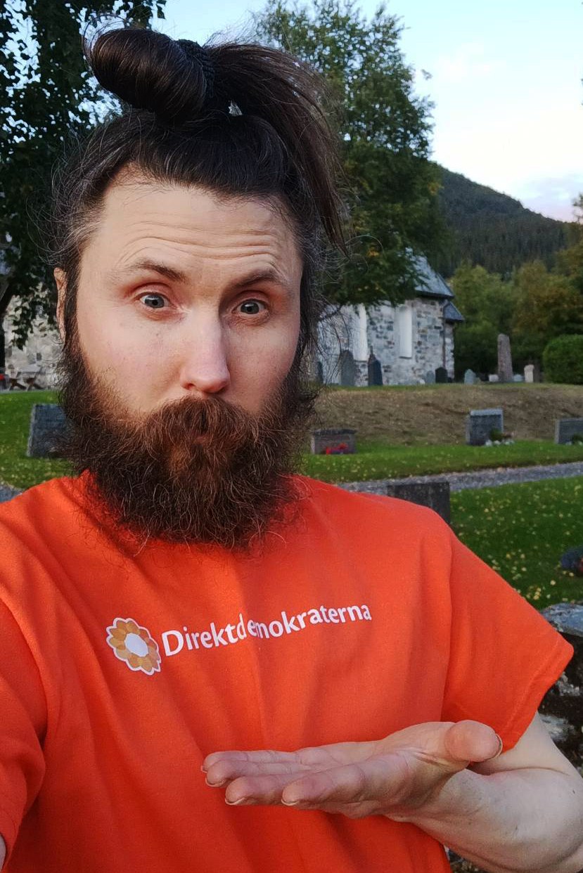 Lukas Hedin i orange Direktdemokraterna-tröja framför Åre gamla kyrka